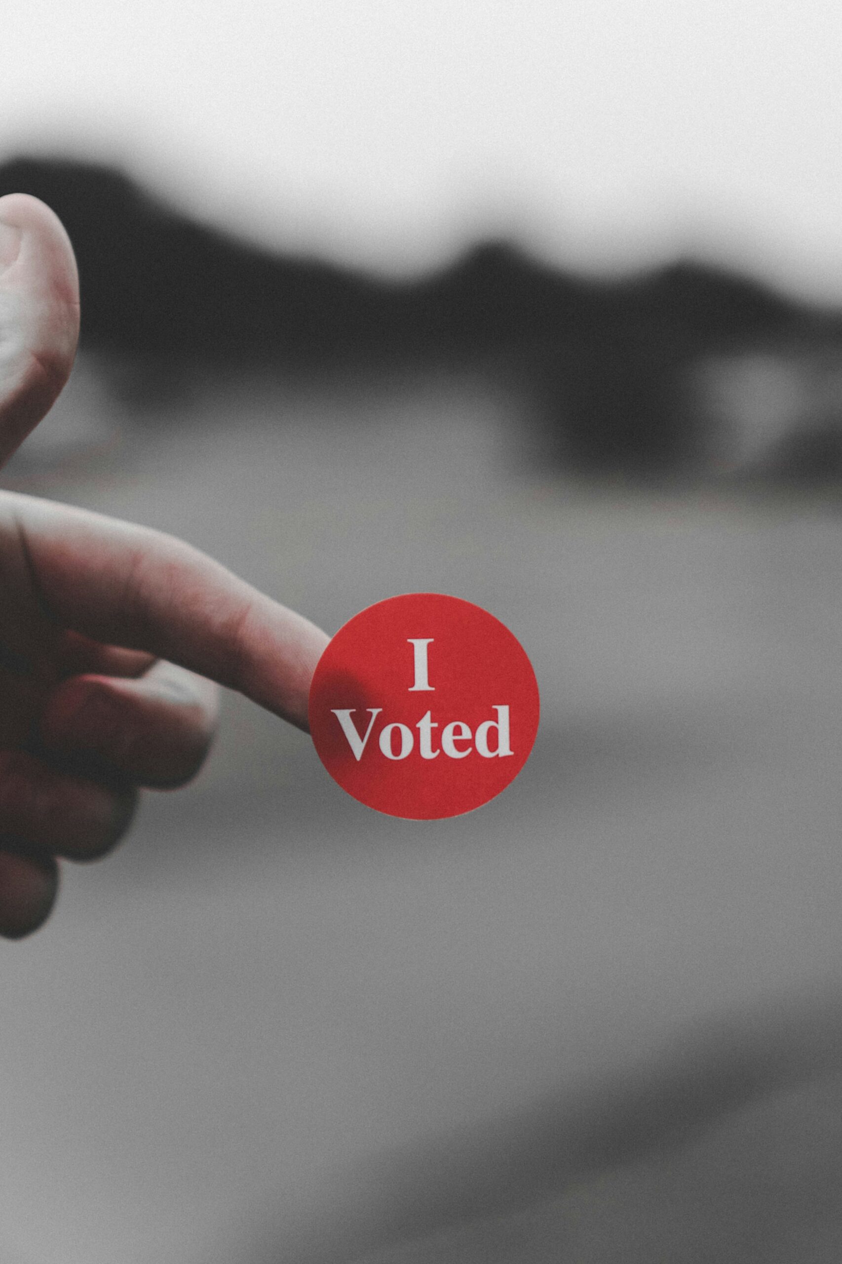 a hand holding a red button that says i vote